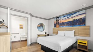 Een moderne hotelkamer met een groot bed, een stadsgezicht schilderij, een ronde spiegel, een houten nachtkastje en een bureau met een stoel.