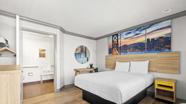 Een moderne hotelkamer met een groot bed, een stadsgezicht schilderij, een ronde spiegel, een houten nachtkastje en een bureau met een stoel.