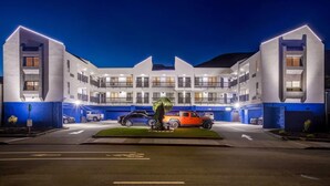 Een hotel met meerdere verdiepingen, een centrale binnenplaats, een parkeerplaats en een goed verlichte gevel.