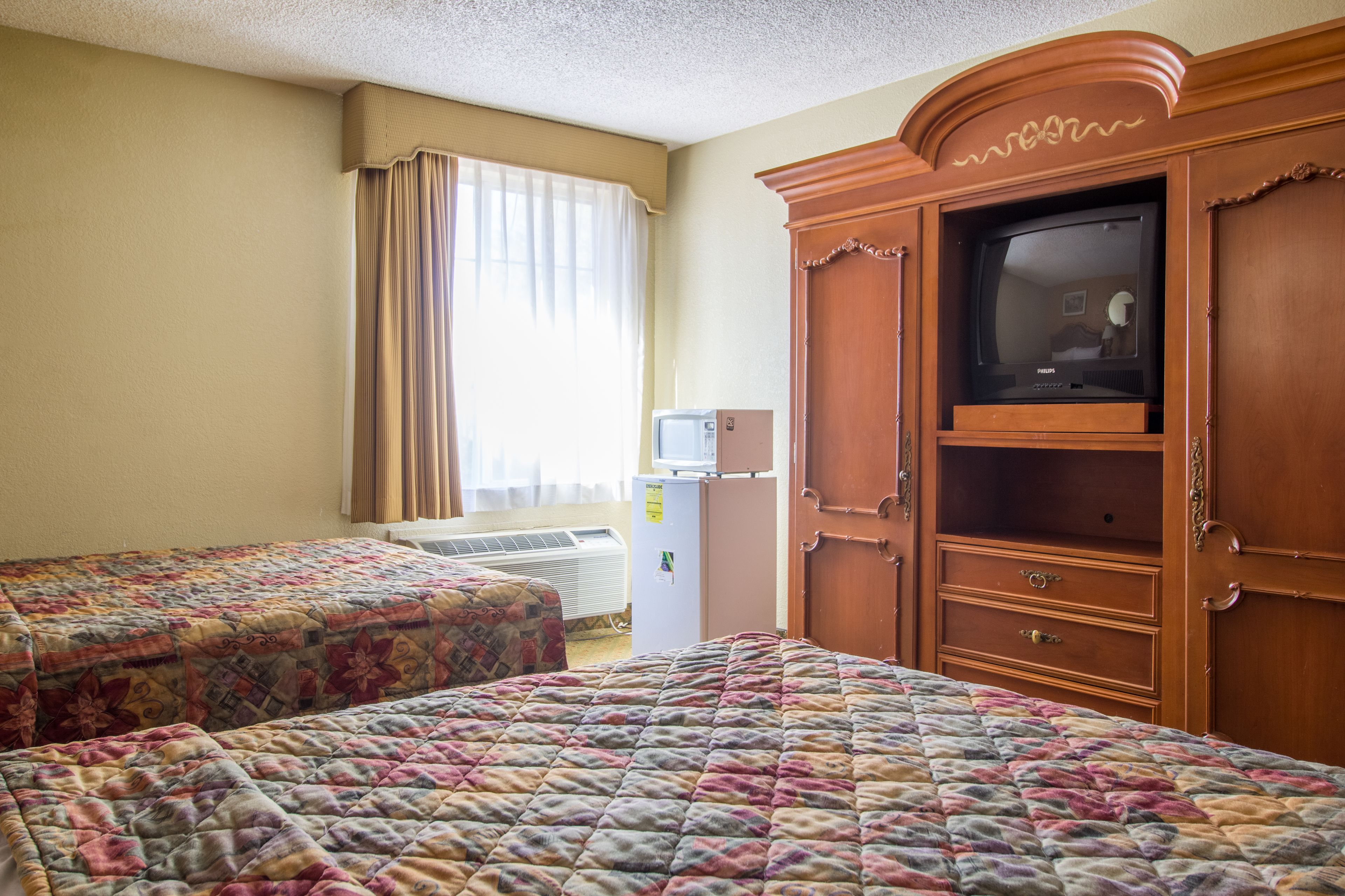 Habitación de hotel con dos camas, televisión, armario y ventana con cortinas.