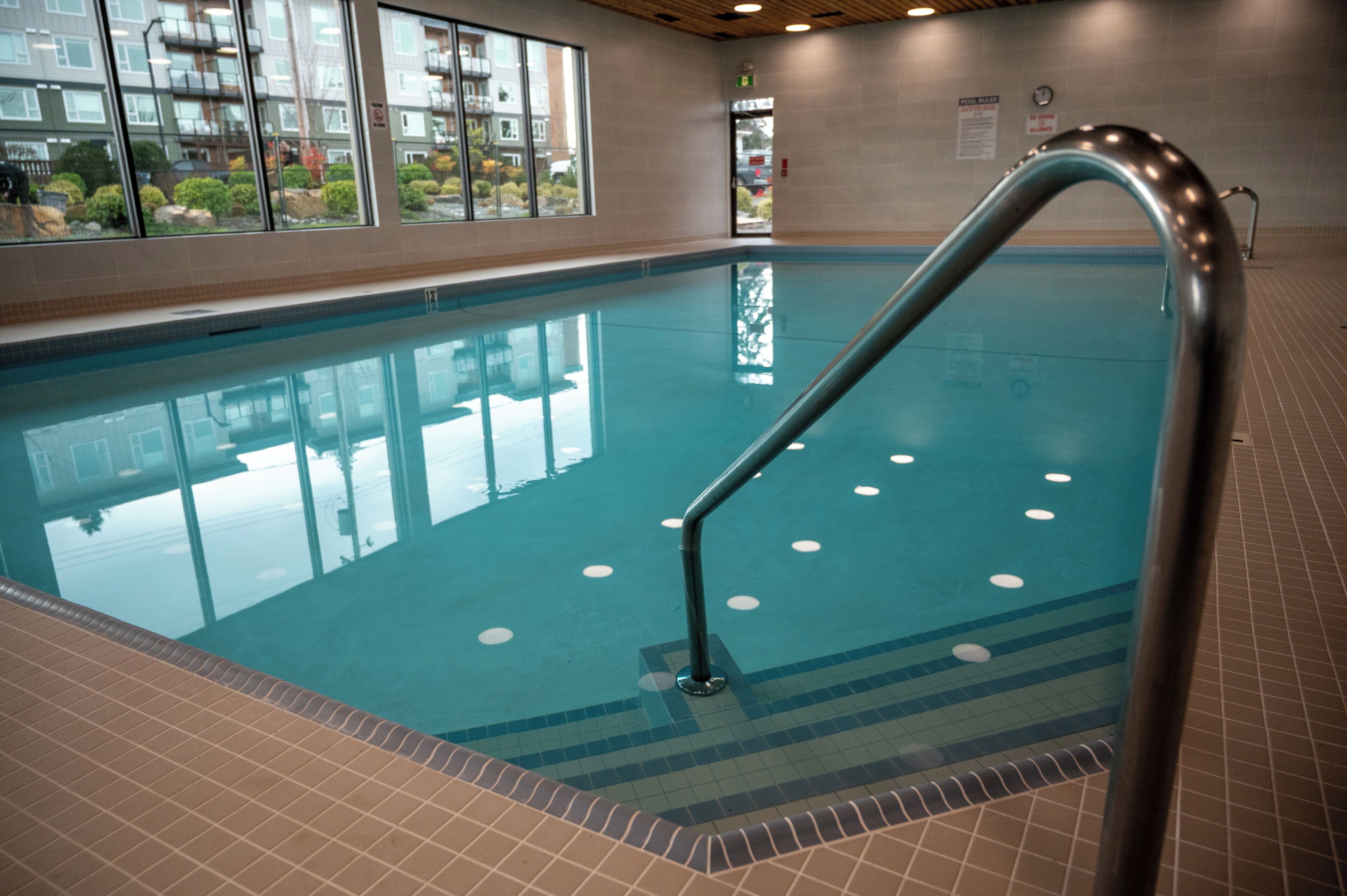 An indoor swimming pool with clear water, a metal handrail, and a tiled floor.
