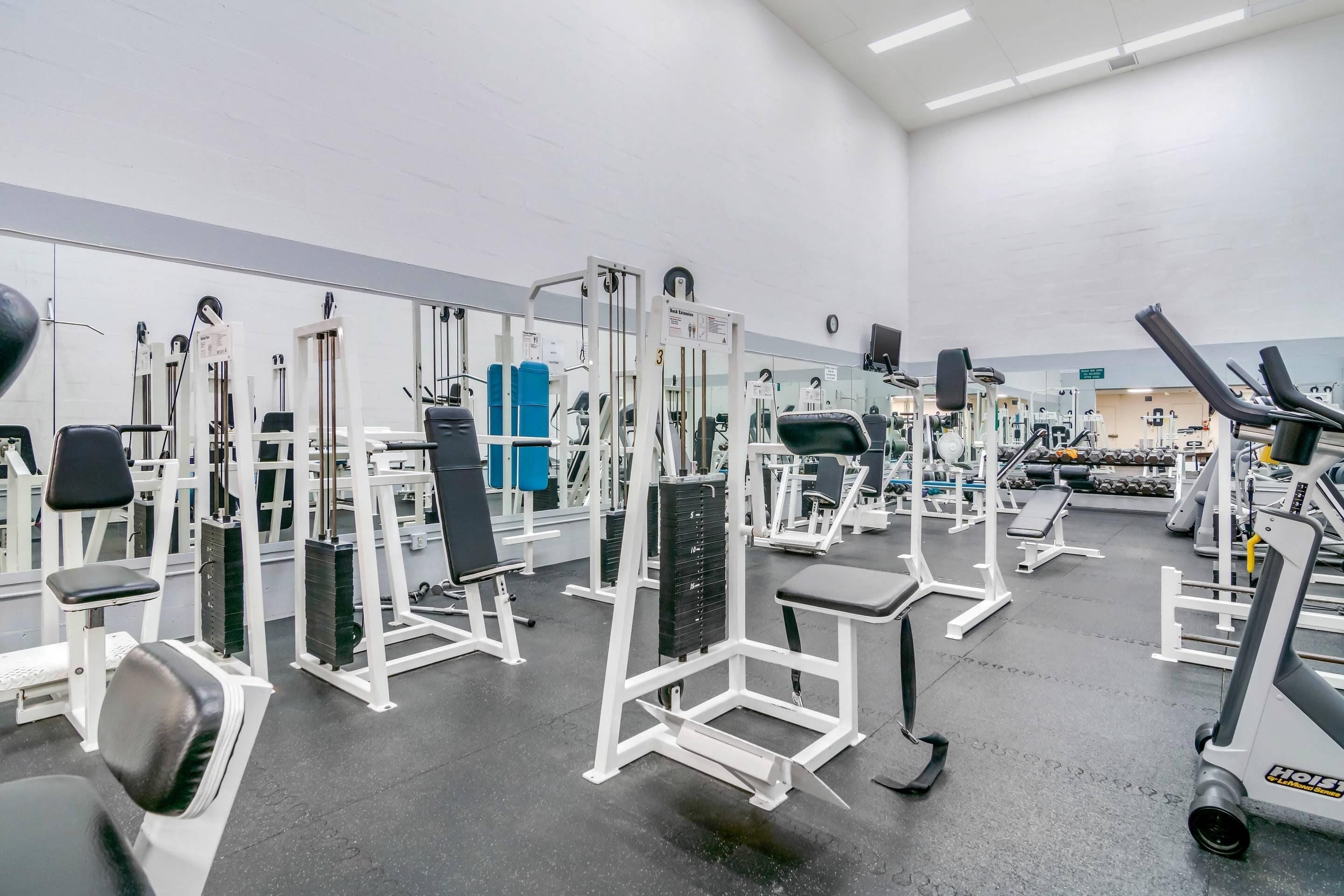 Un gimnasio con diferentes máquinas de ejercicio, espejos y pesas.