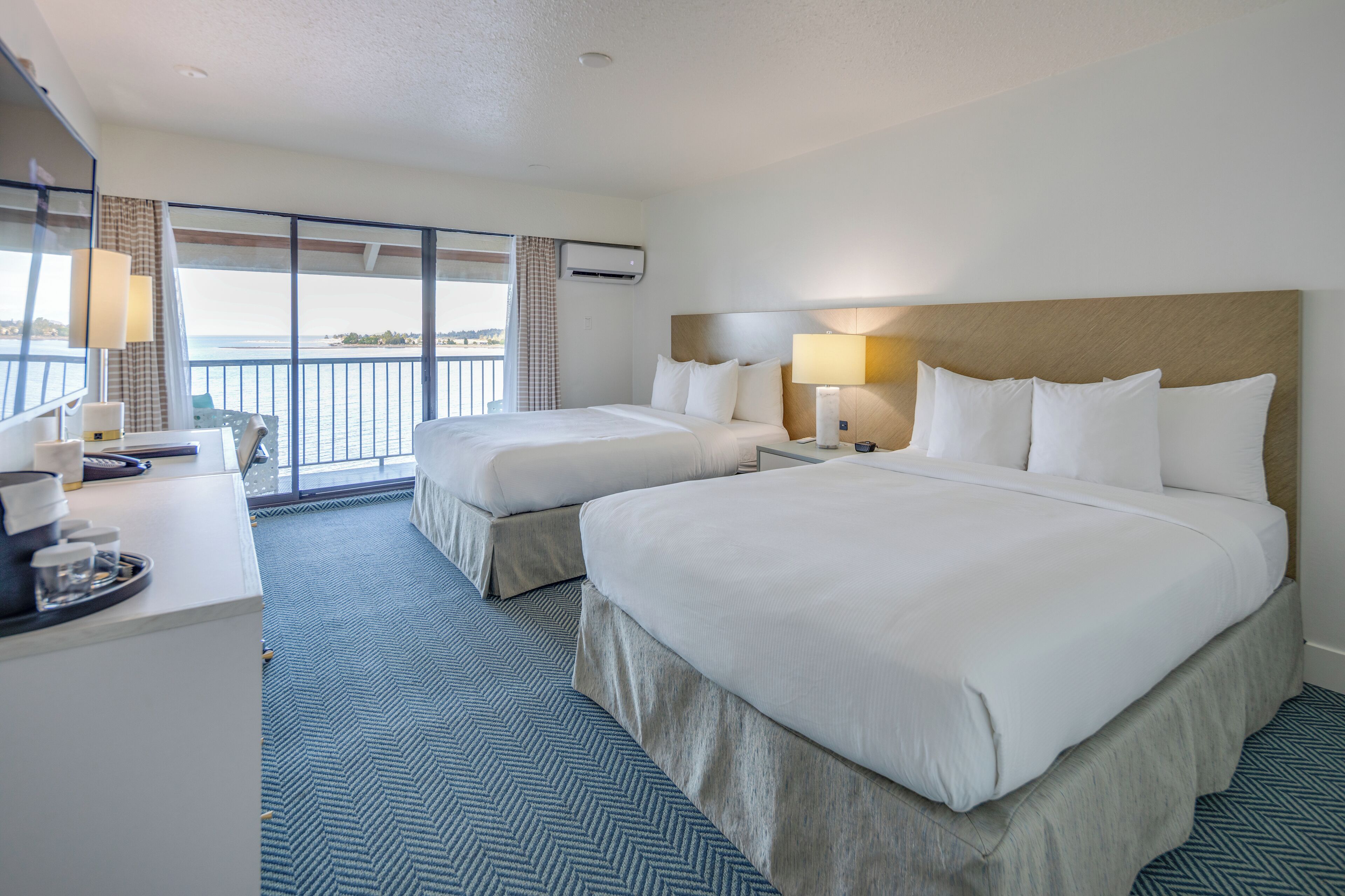 A hotel room with two beds, a desk, and a balcony with a view.