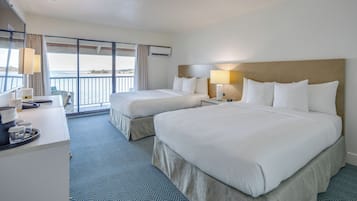 A hotel room with two beds, a desk, and a balcony with a view.