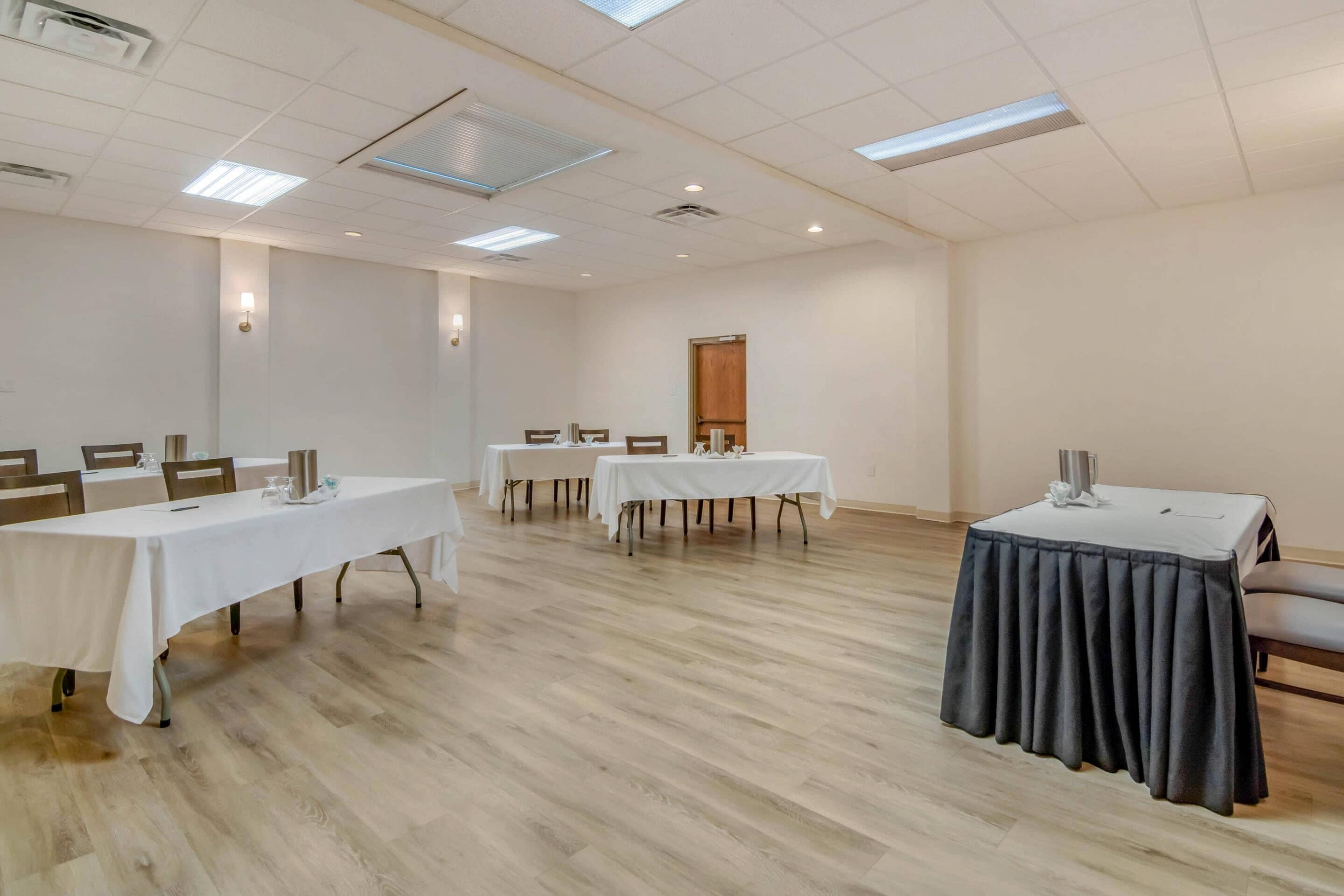 A conference room with multiple tables, chairs, and a wooden floor.