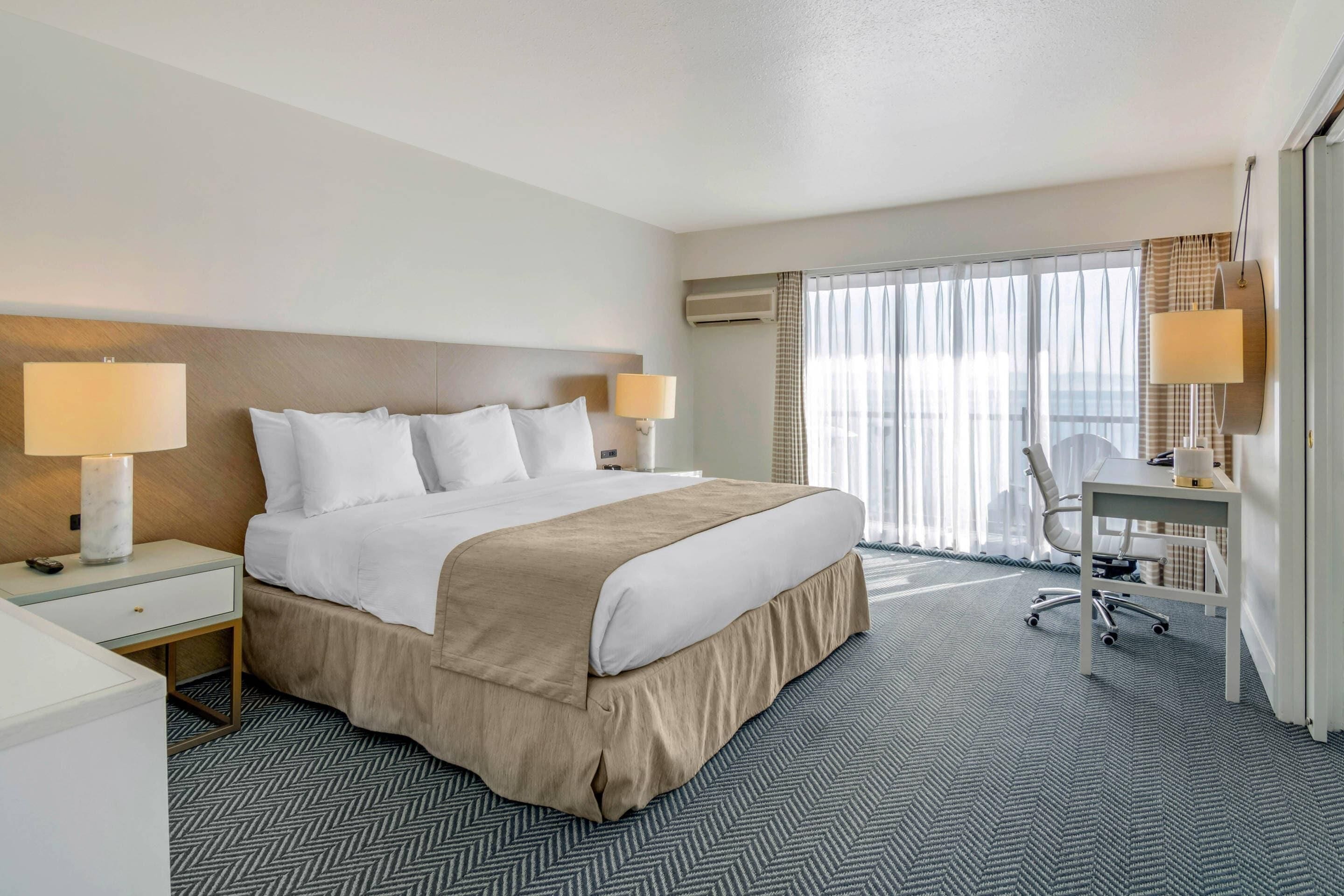 Habitación de hotel con una cama grande, dos lámparas de noche, un escritorio con silla y vistas al exterior a través de la ventana.