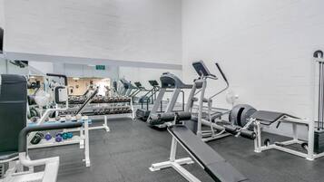 Ett gym med olika typer av träningsutrustning, inklusive löpband, styrketräningsmaskiner och hantlar.
