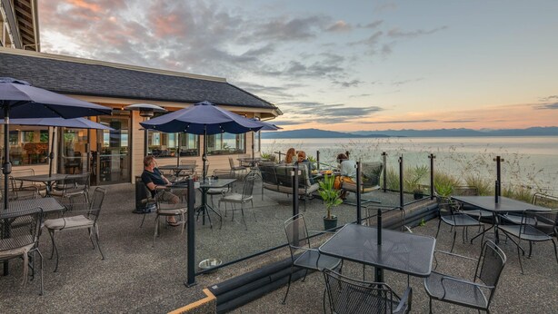 An outdoor patio with tables and chairs, umbrellas, and a view of the water.