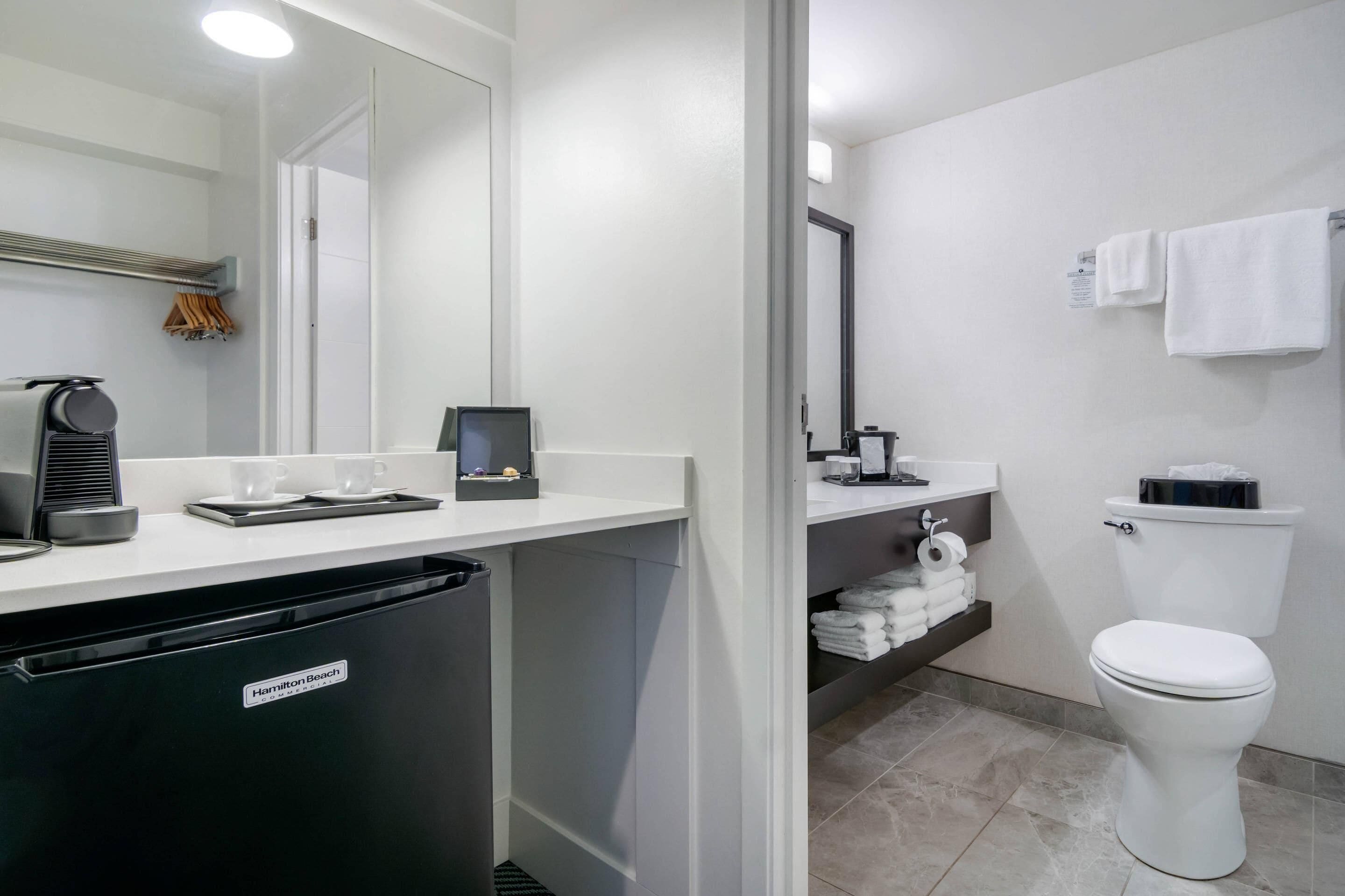 Un baño moderno con un lavavajillas negro, un lavamanos con una cafetera y un inodoro.