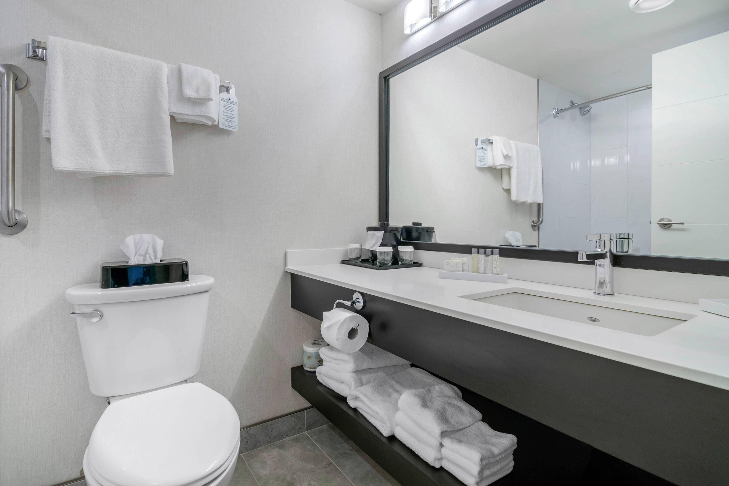 A modern bathroom with a toilet, sink, and large mirror. There are towels and toiletries on the counter.