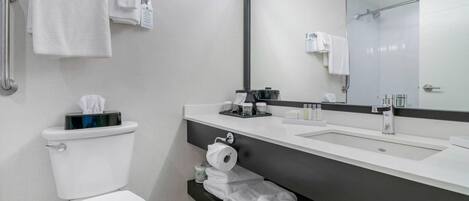 A modern bathroom with a toilet, sink, and large mirror. There are towels and toiletries on the counter.