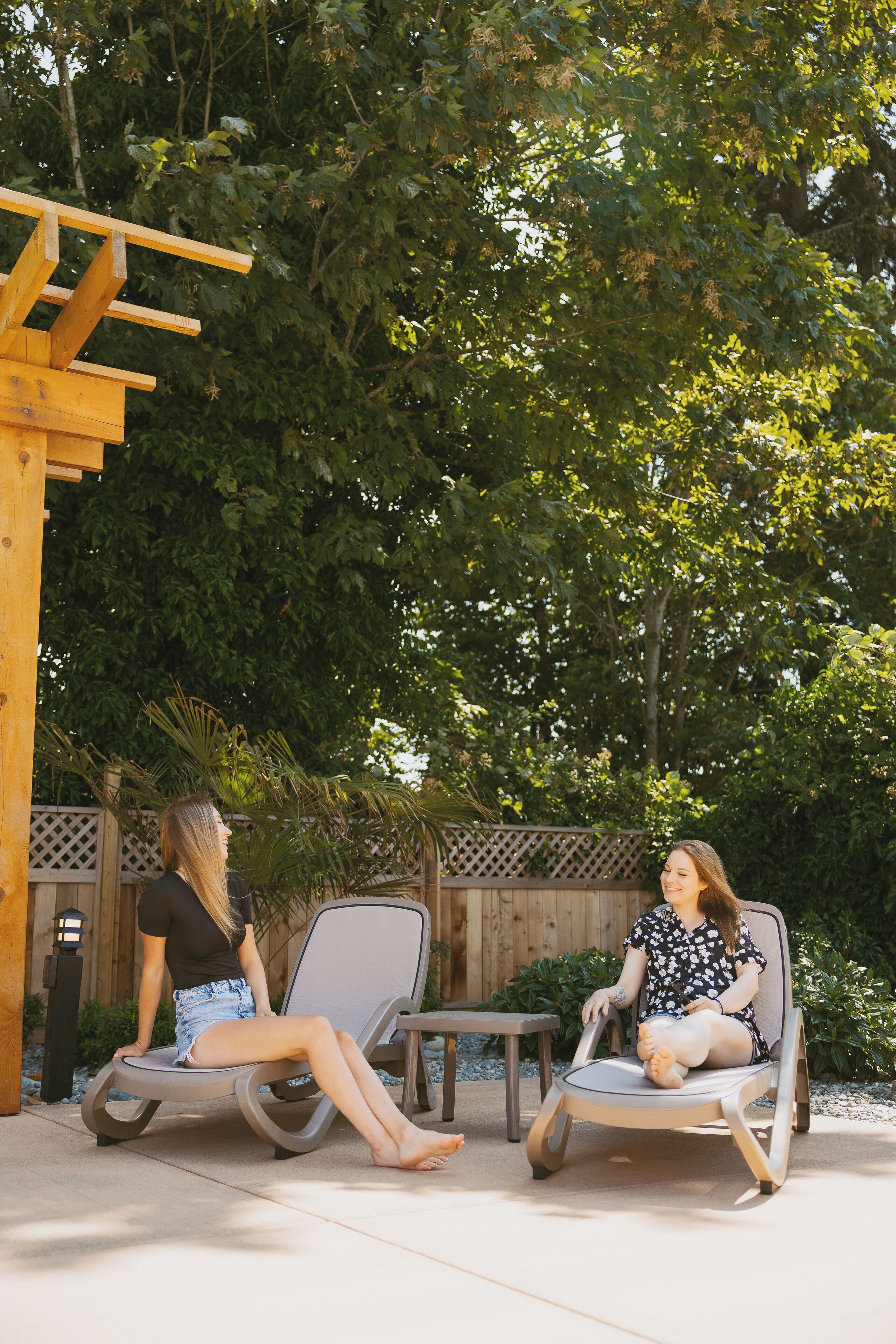 Deux fauteuils de jardin sont disposés dans un espace extérieur aménagé en patio, avec une pergola en bois et une clôture en bois en arrière-plan.