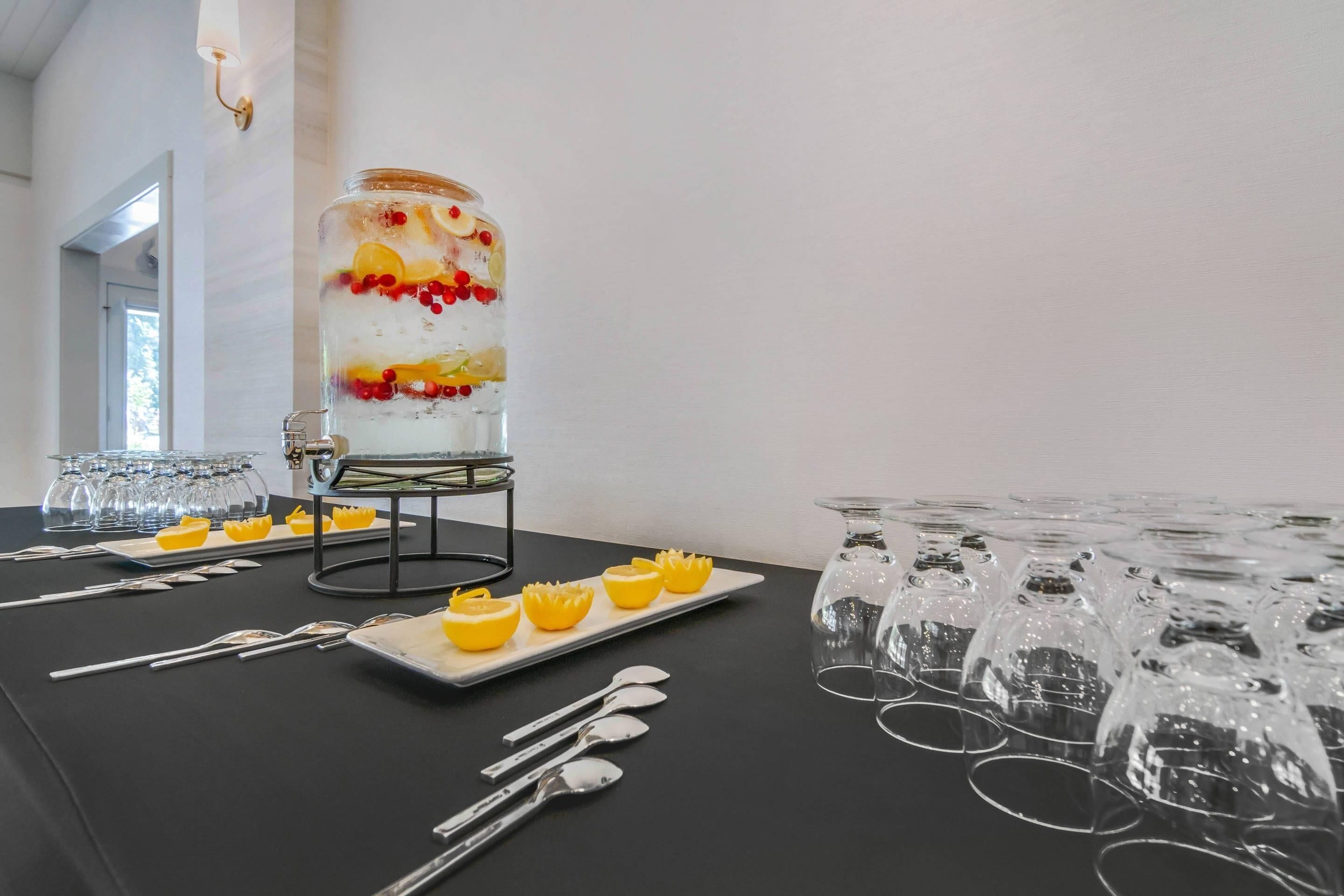 A table set with clear glasses, a large jar with layered contents, and yellow fruit slices.