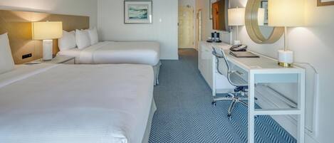 A hotel room with two beds, a desk with a chair, a desk lamp, a telephone, and a mirror.
