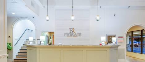 A reception area with a central desk, a staircase on the left, and a large sign for 'The Bayside Oceanfront Resort' above the desk.