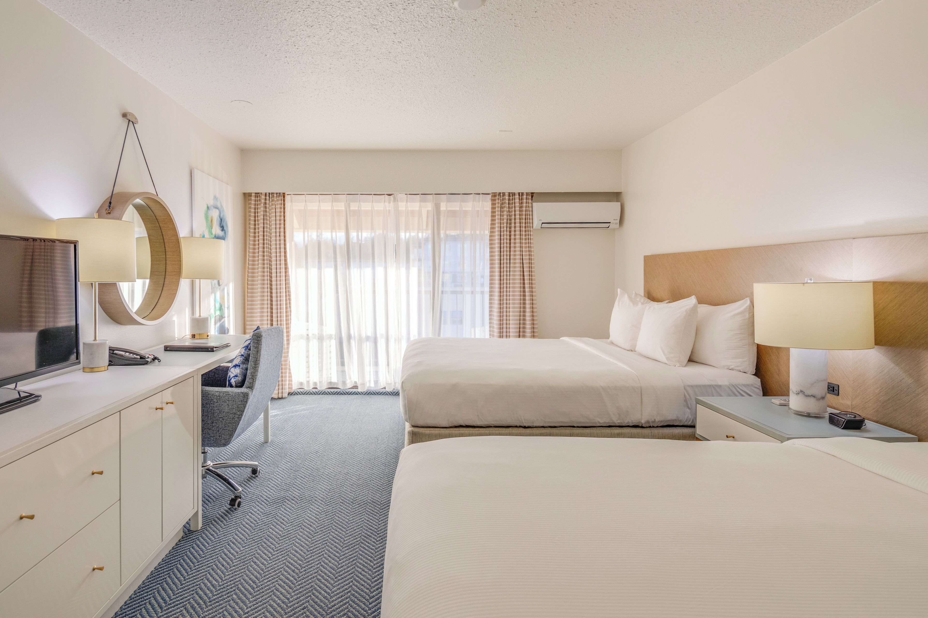 A hotel room with a bed, a desk with a computer, a chair, and a TV.