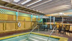 An indoor swimming pool with steps leading into it, surrounded by tables and chairs under a covered area. - Howard Johnson by Wyndham Santa Cruz (Santa Cruz)