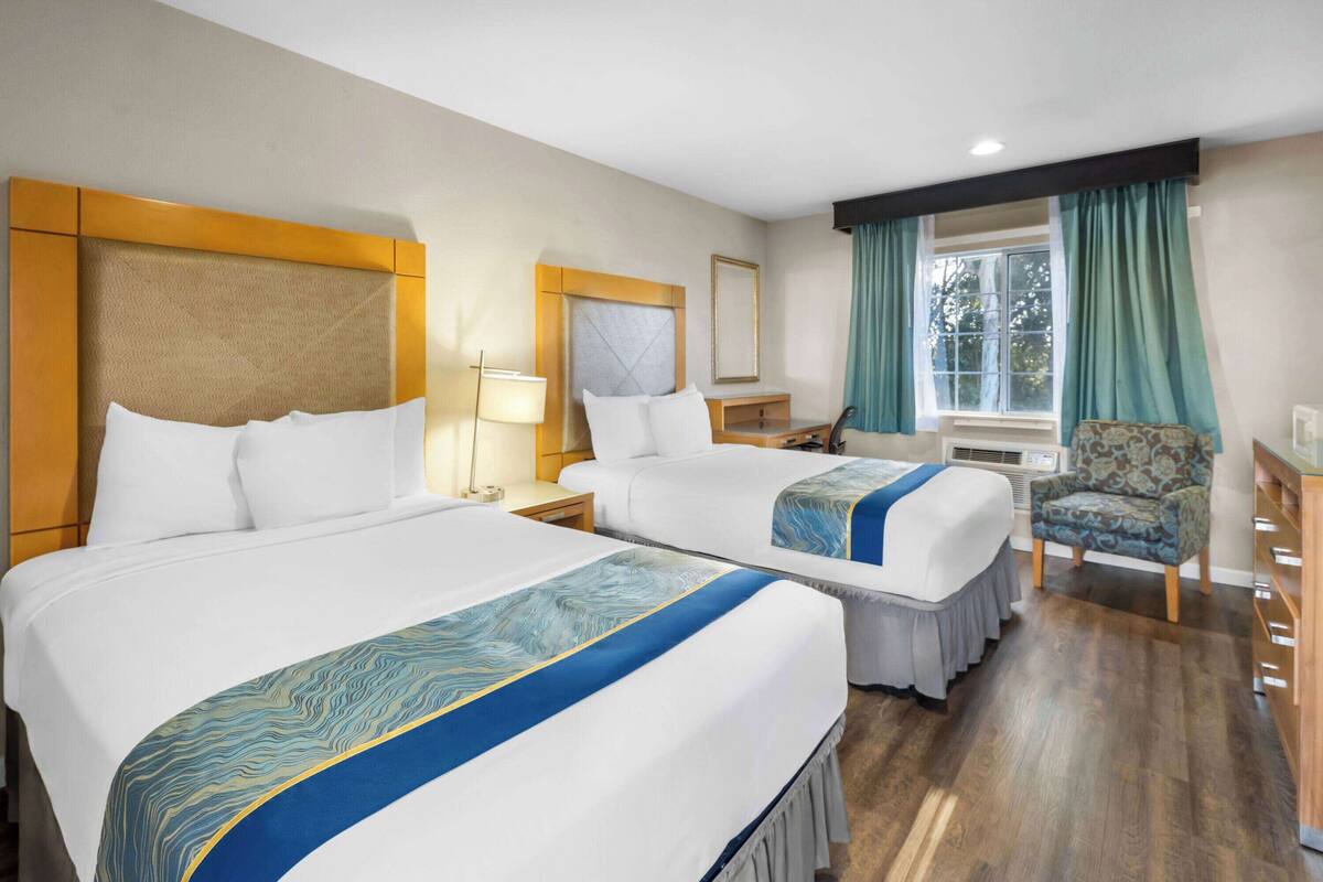 Een hotelkamer met twee bedden, een stoel, een bureau en een raam met gordijnen.