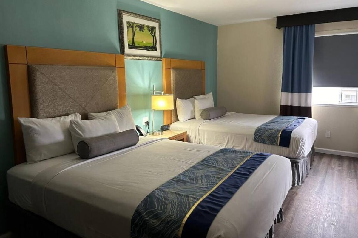 Een hotelkamer met twee bedden, een nachtkastje, een lamp en een raam met gordijnen.