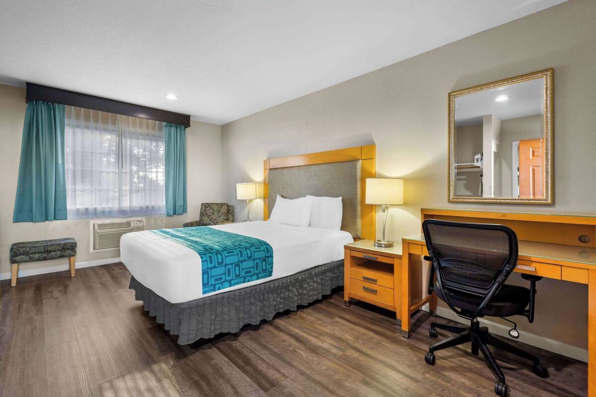 Een hotelkamer met een groot bed, nachtkastjes, een bureau, een stoel en een spiegel.