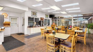 A restaurant with wooden tables and chairs, a kitchen area, and a large window with a view. - Howard Johnson by Wyndham Santa Cruz (Santa Cruz)