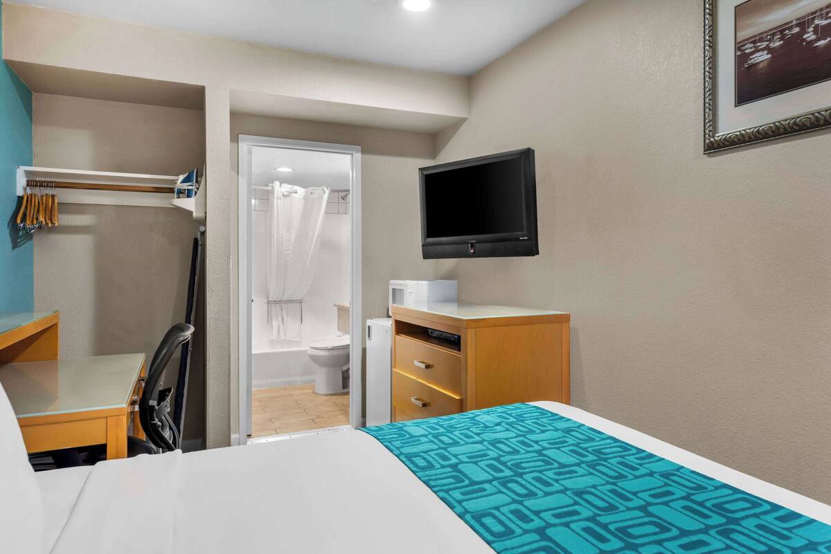 Hotelkamer met een bed, bureau, stoel, televisie, kledingkast en douche.