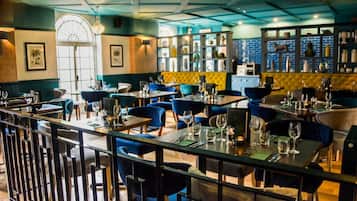A restaurant with multiple tables and chairs, a bar area with shelves of bottles, and framed pictures on the walls.