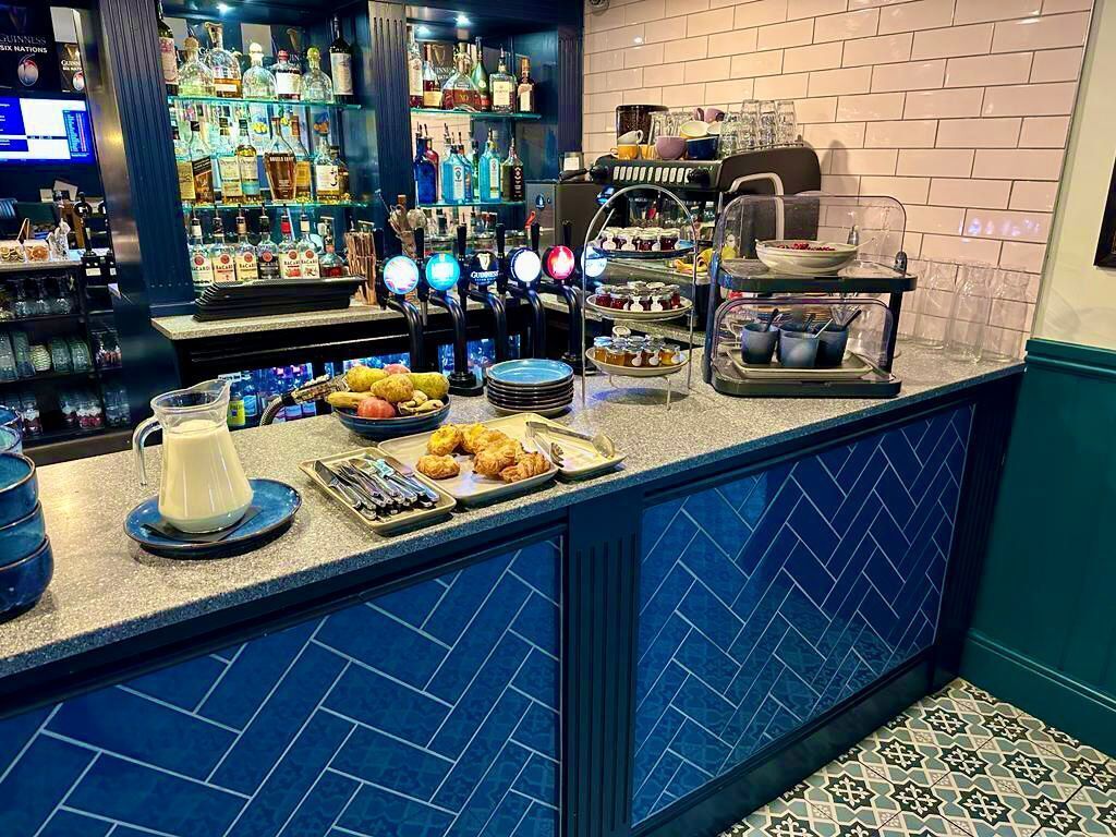 A bar area with a counter displaying food items, a variety of liquor bottles, and a coffee machine.