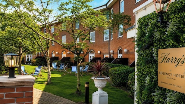 A brick building with a sign for Harry's at Regency Hotel, a well-maintained lawn, and blue-striped lounge chairs.
