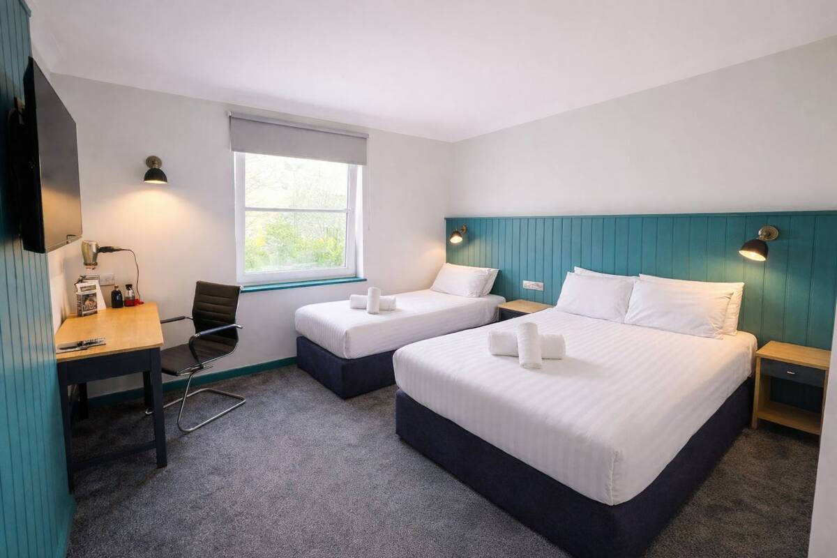Ein Hotelzimmer mit zwei Betten, einem Schreibtisch, einem Sessel, einem Fernseher und einem Fenster.