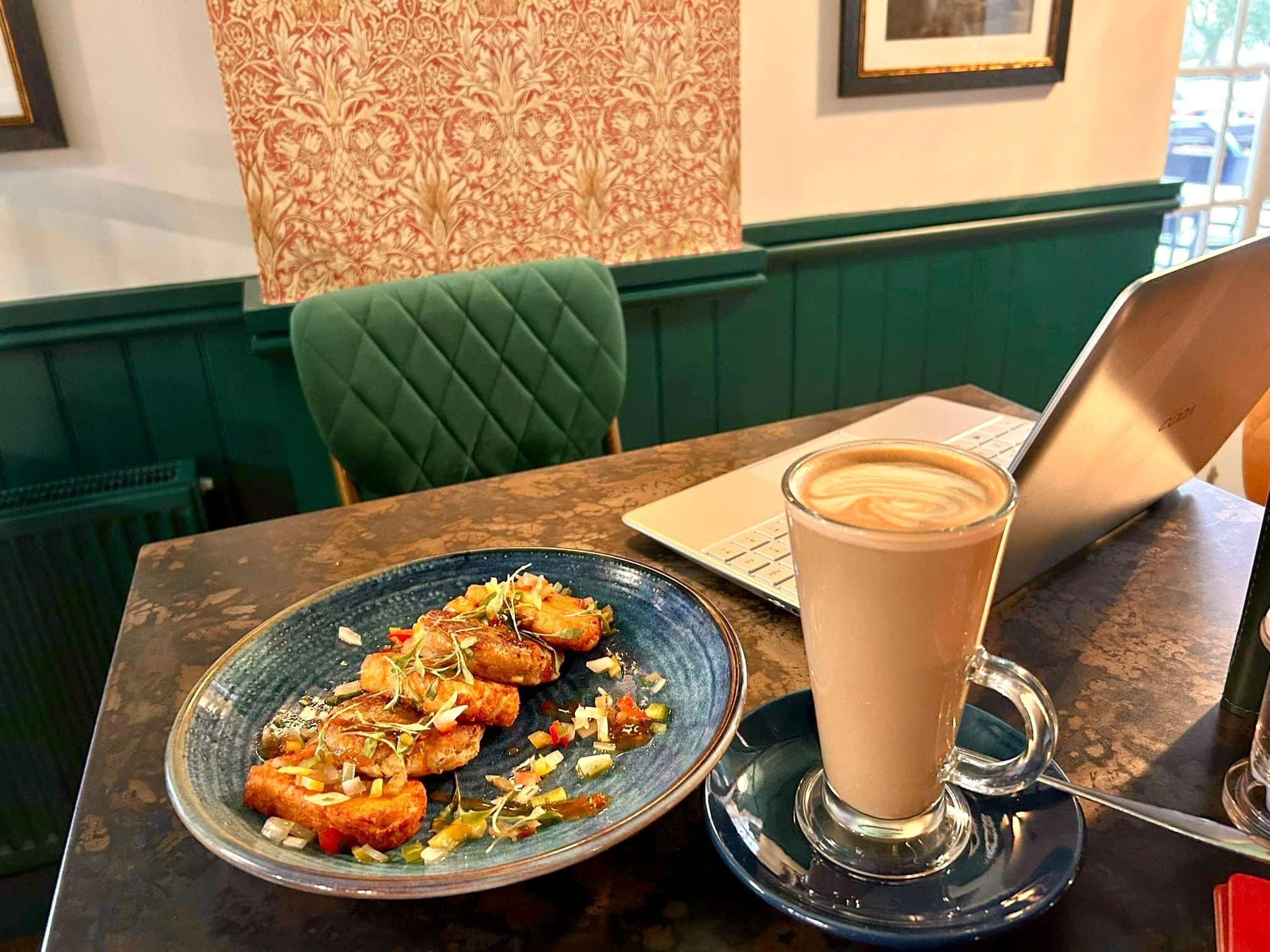 Uma mesa de jantar com um laptop, um prato de comida e uma xícara de café.