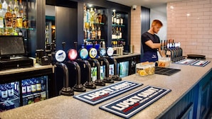 A bar area with multiple beer taps, a digital screen, and a counter with branded coasters.