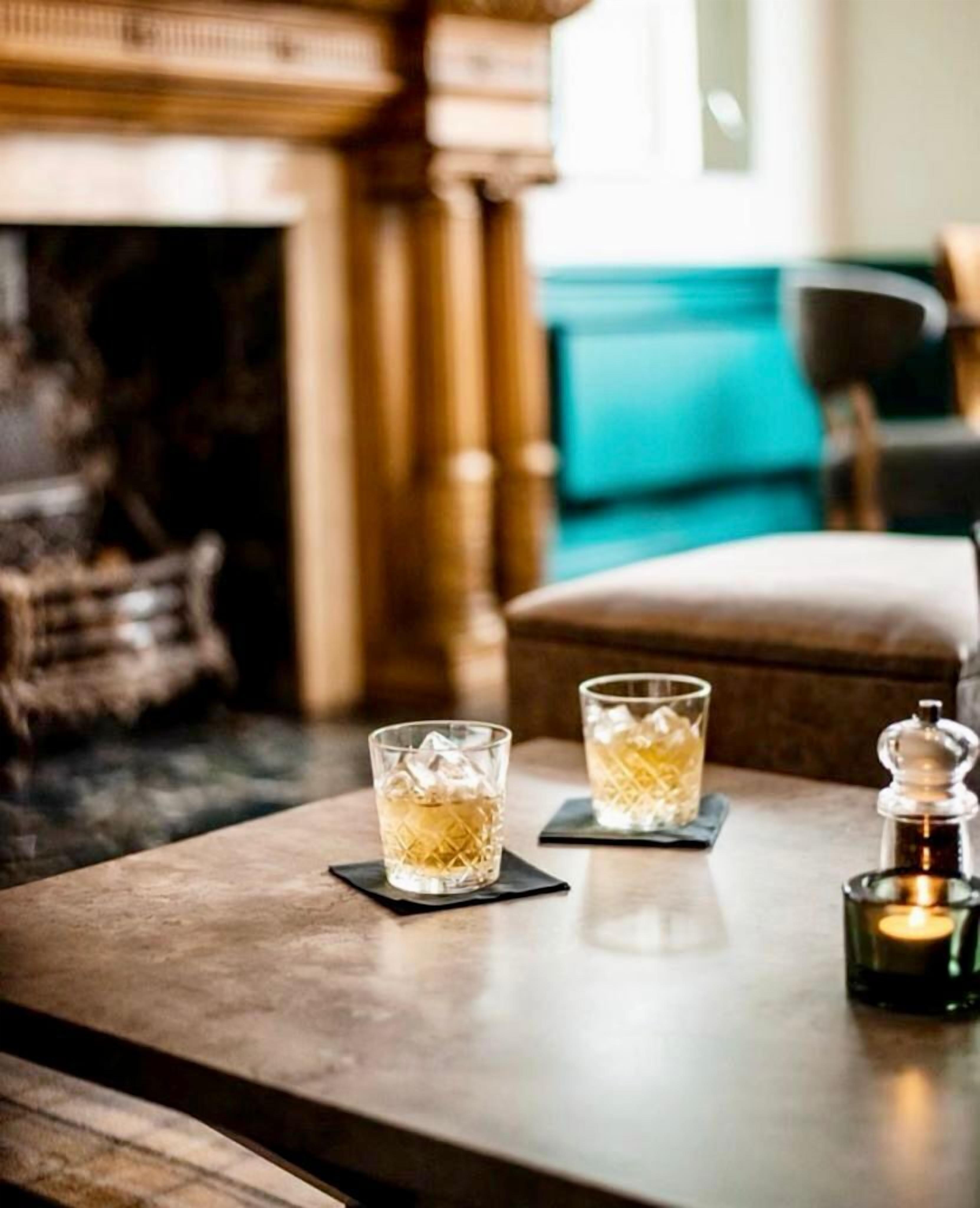 A table with two glasses of a clear liquid, possibly a beverage, with ice cubes. There is a candle in a glass holder on the table.