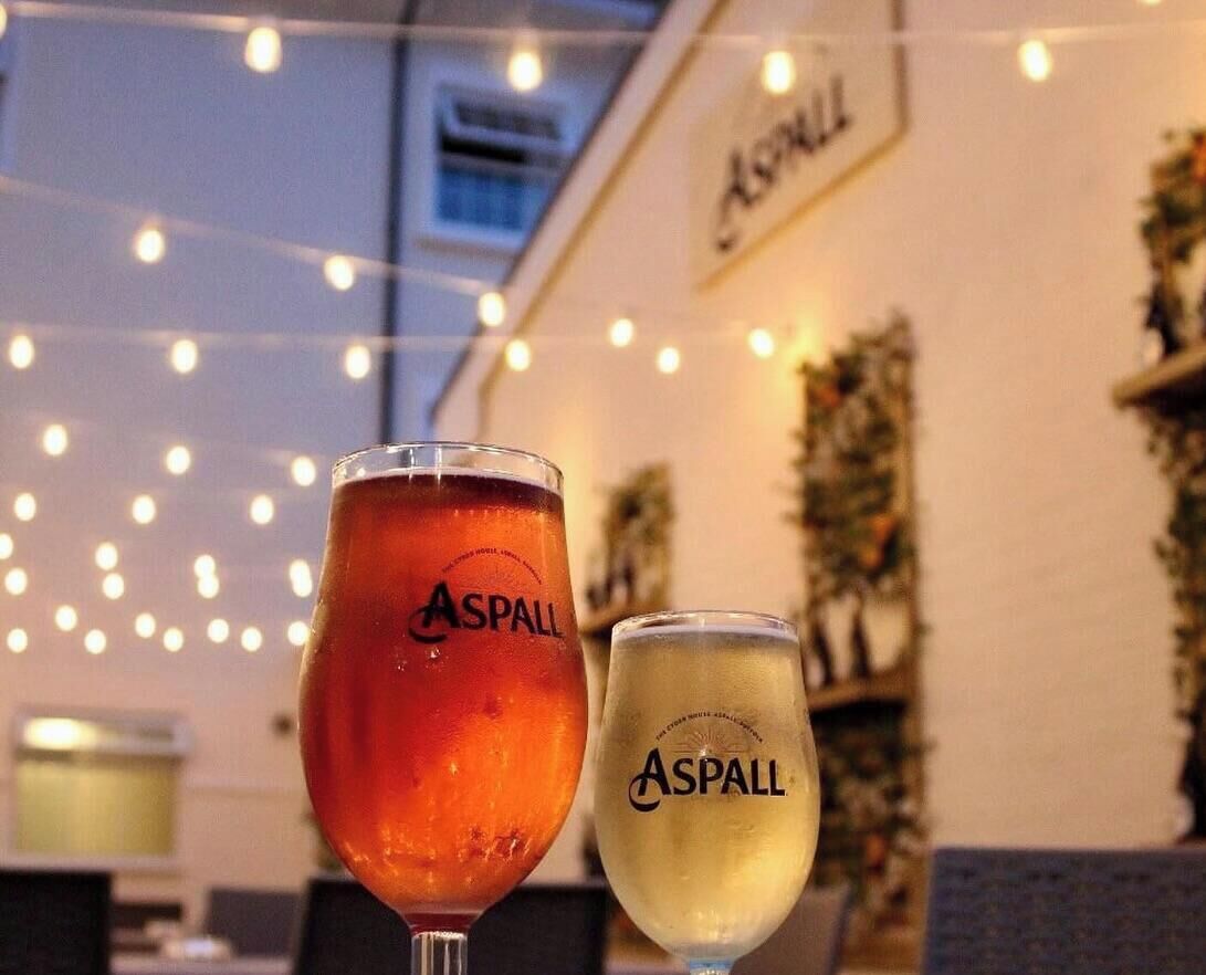 Dos vasos de cerveza Asphall, uno roja y otro blanca, sobre una mesa con luces de cuerda al fondo.
