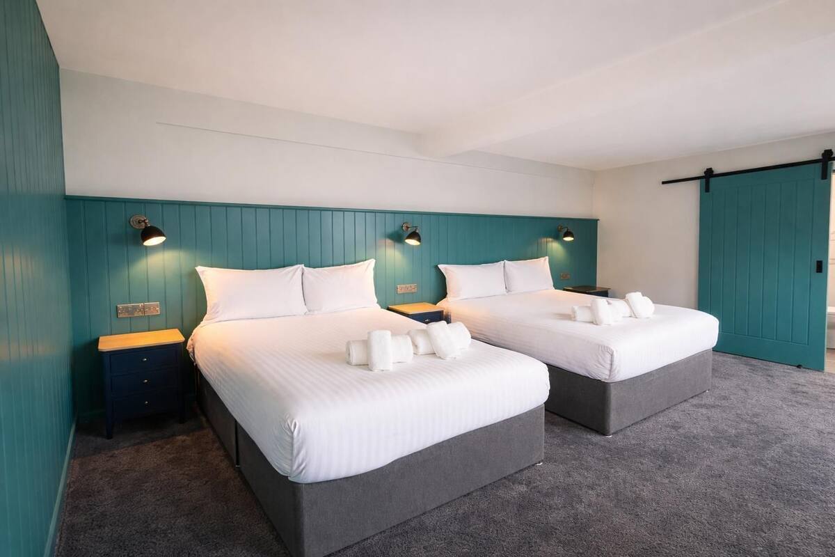 Ein Doppelzimmer mit zwei Betten, türkisfarbenen Wänden und Nachttischlampen.