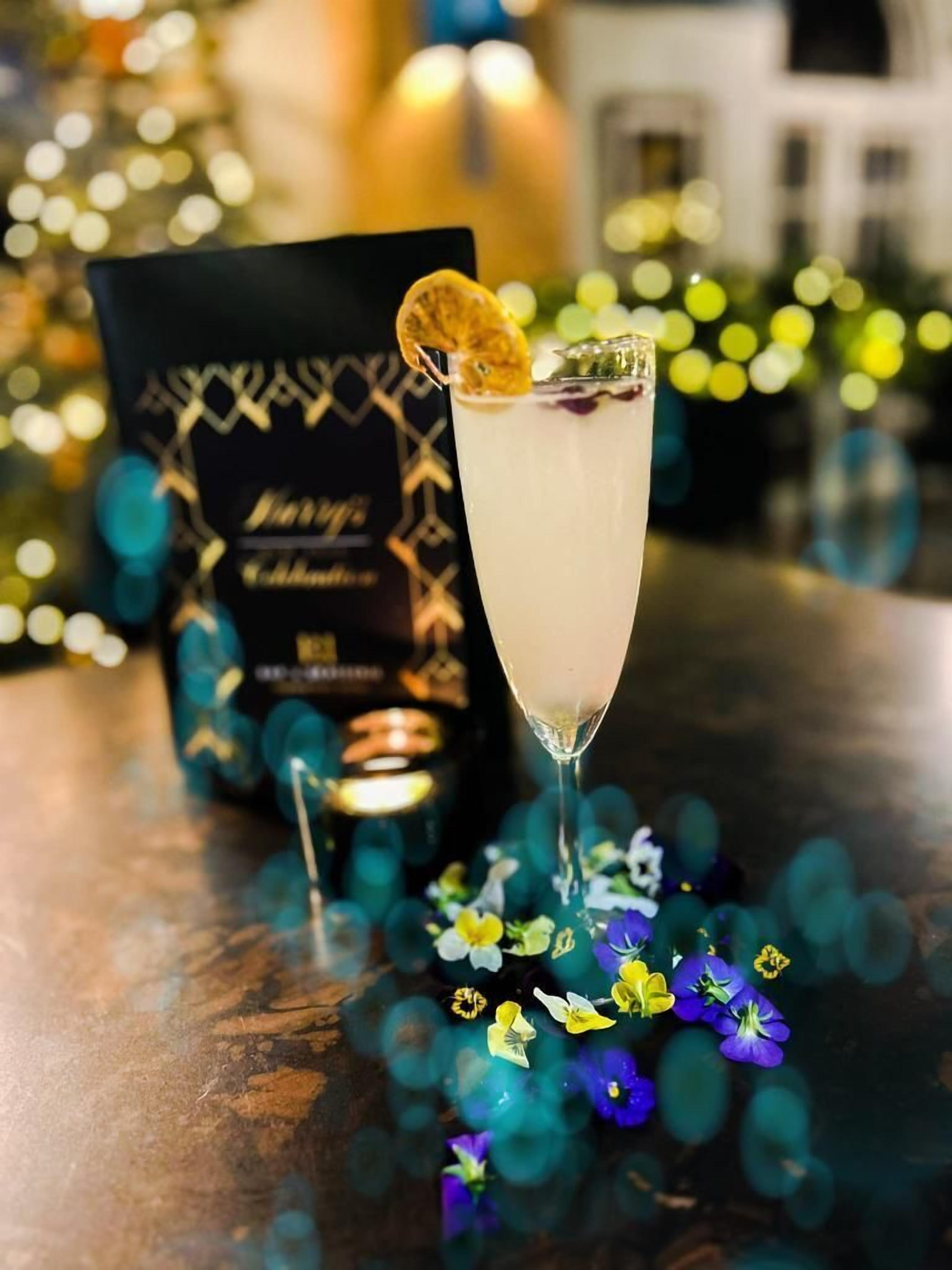A cocktail glass with a garnish, a bottle, and a menu on a table with flowers.