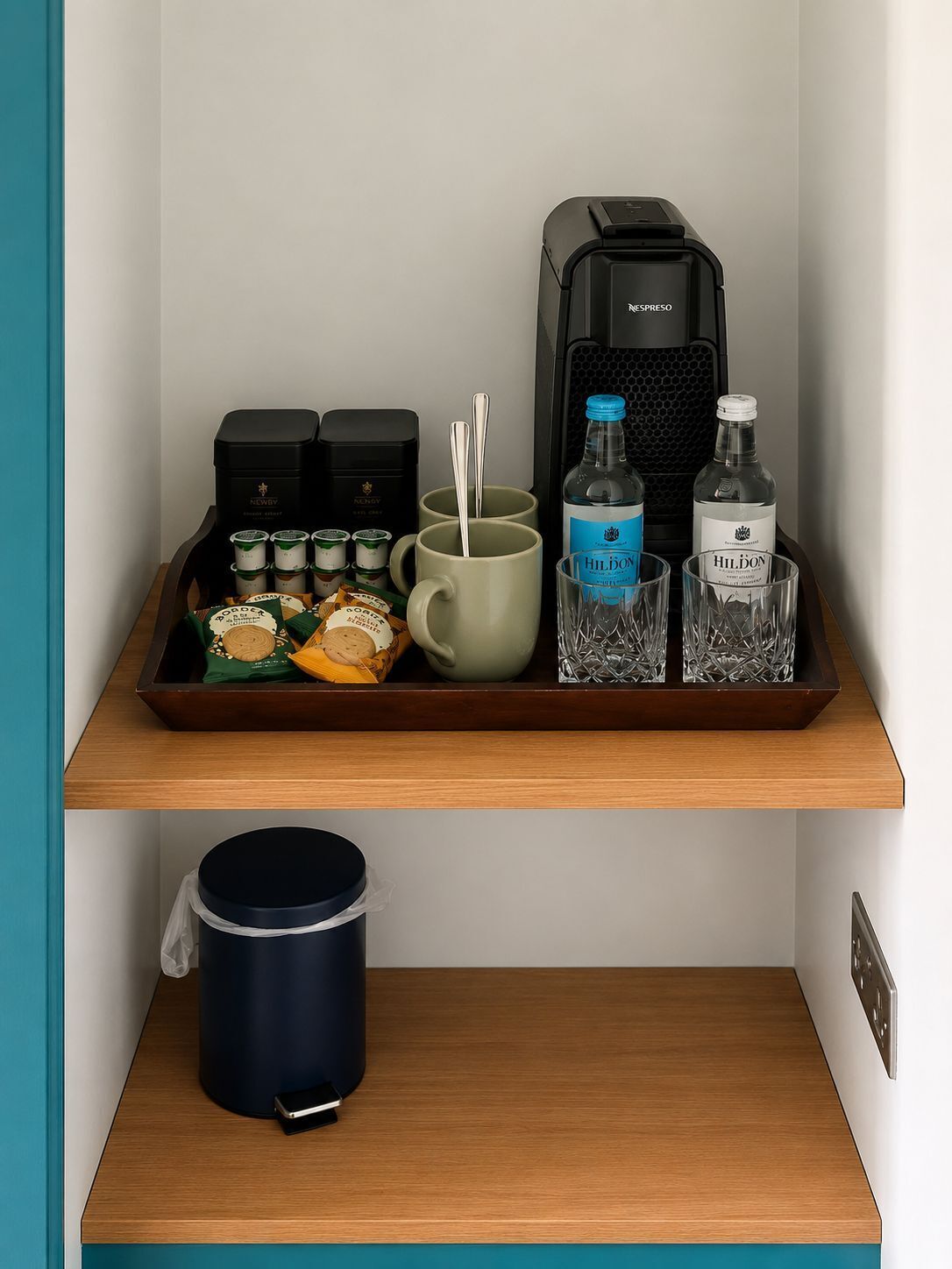 A tray with a coffee maker, mugs, and bottles on a shelf.