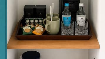 A tray with a coffee maker, mugs, and bottles on a shelf.