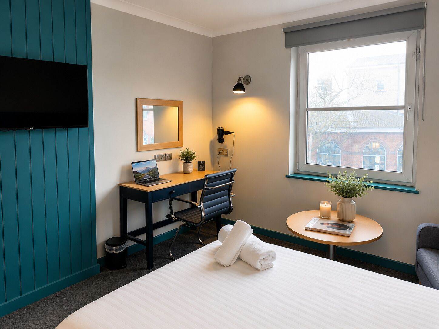 Habitación de hotel con escritorio, silla, cama, mesita de noche y ventana con vistas.