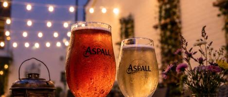 Dos vasos de cerveza con el logotipo 'Aspall', un farol y un jarrón con flores sobre una mesa.