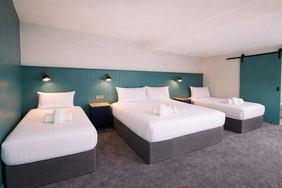 Ein Hotelzimmer mit drei Betten, türkisfarbenen Wänden und einem grauen Teppich.