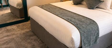 A neatly arranged hotel room with a large bed, a bedside table, a mirror, and a wall-mounted light fixture.