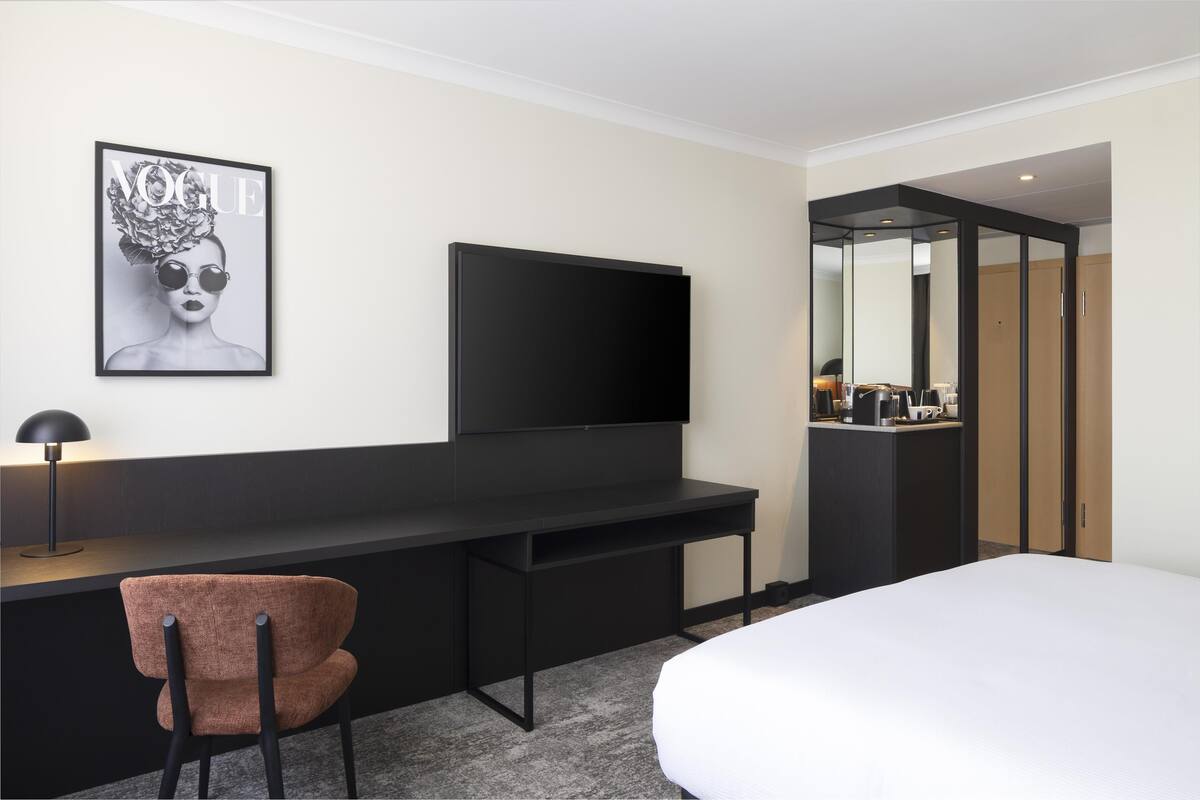 Een moderne hotelkamer met een groot bed, een bureau met een flatscreen televisie, een stoel en een minibar.