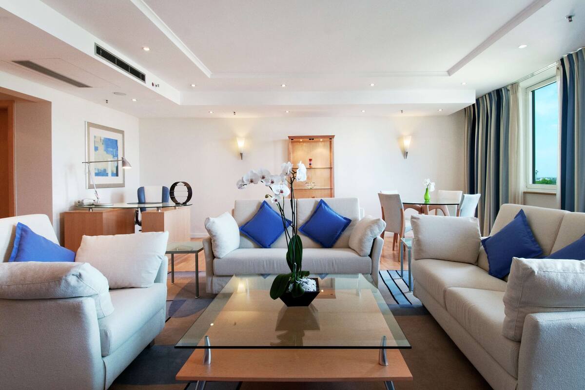 Een moderne woonkamer met een glazen salontafel, witte banken met blauwe kussens en een decoratieve orchidee als middelpunt.