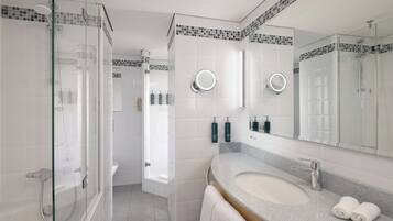 Un baño moderno con ducha de vidrio, lavamanos con tocador y espejo con luz redonda.