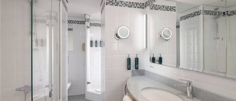 Un baño moderno con ducha de vidrio, lavamanos con tocador y espejo con luz redonda.