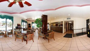 A spacious lobby with a central round table and chairs, a bar area, and a staircase leading to an upper level.