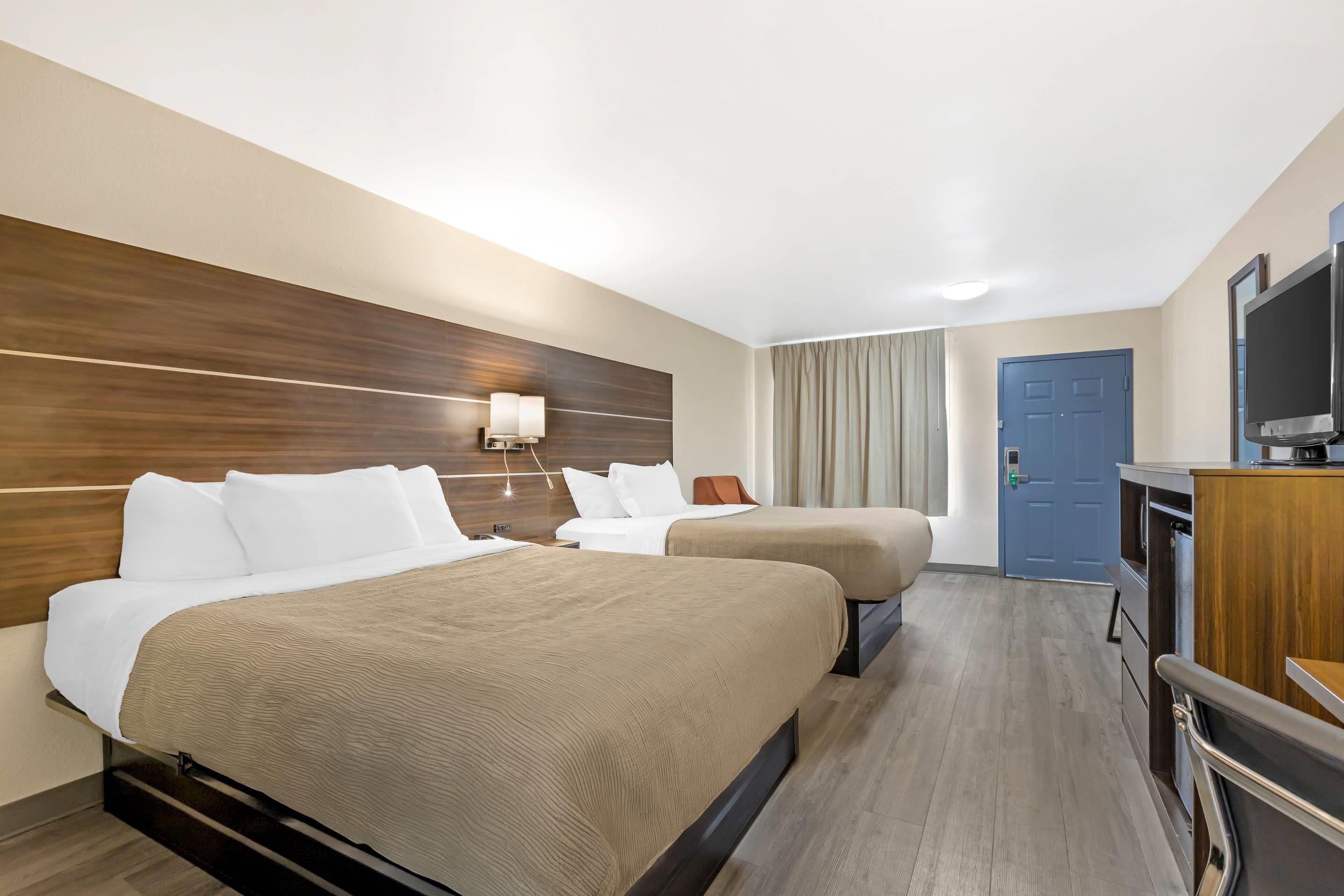A hotel room with two beds, a TV, a desk, and a door.