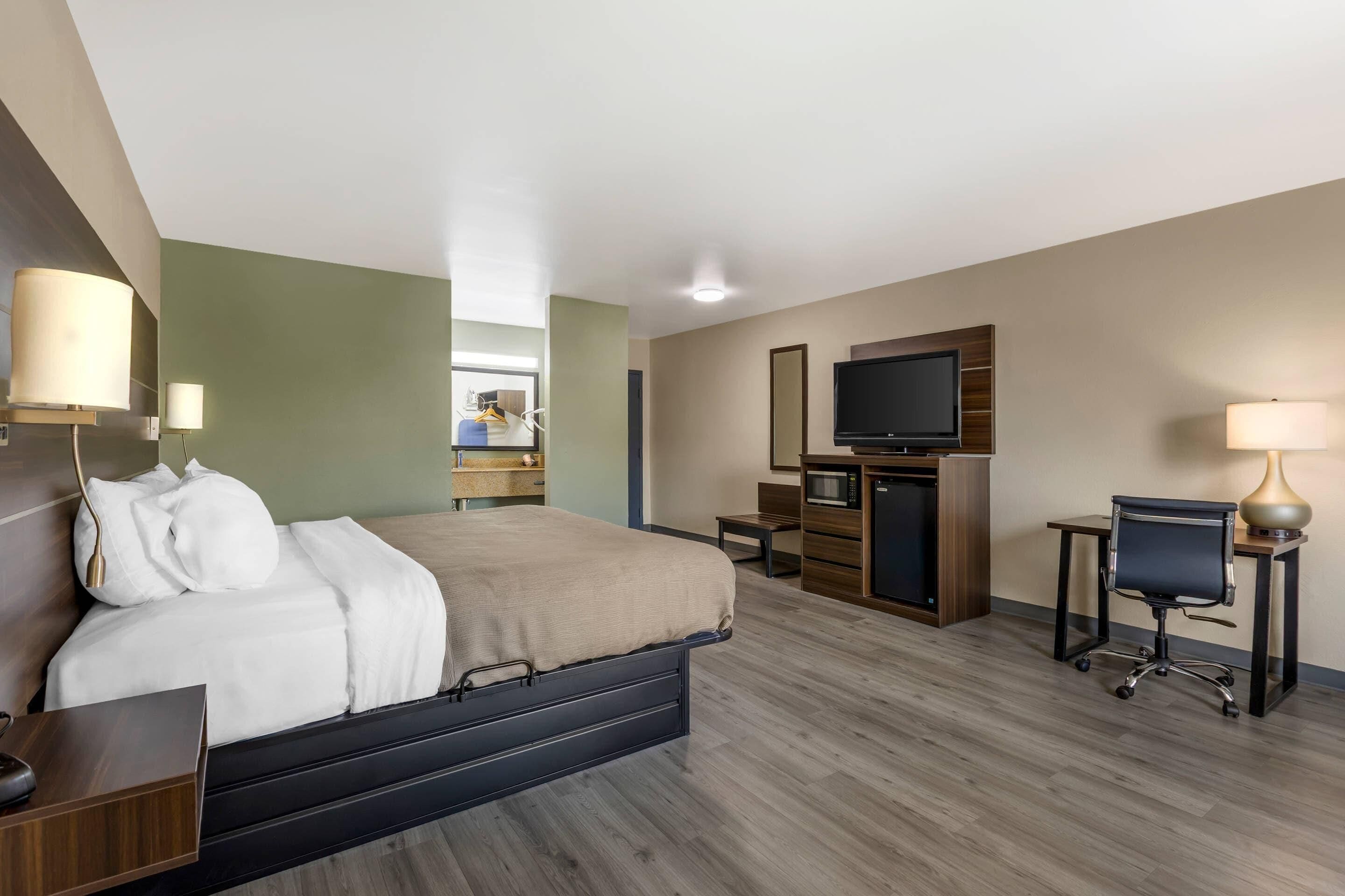 Habitación de hotel con cama, escritorio, televisor y una pequeña kitchenette.