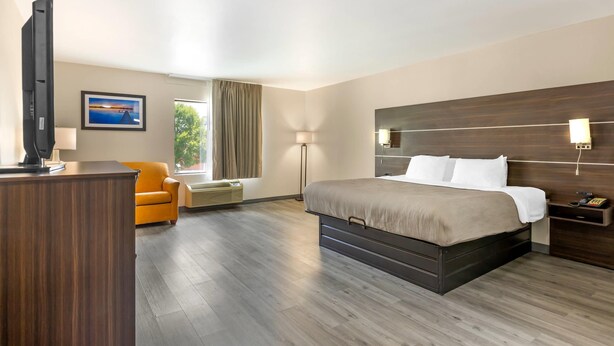 A hotel room with a bed, a desk, a chair, a TV, and a window with curtains.